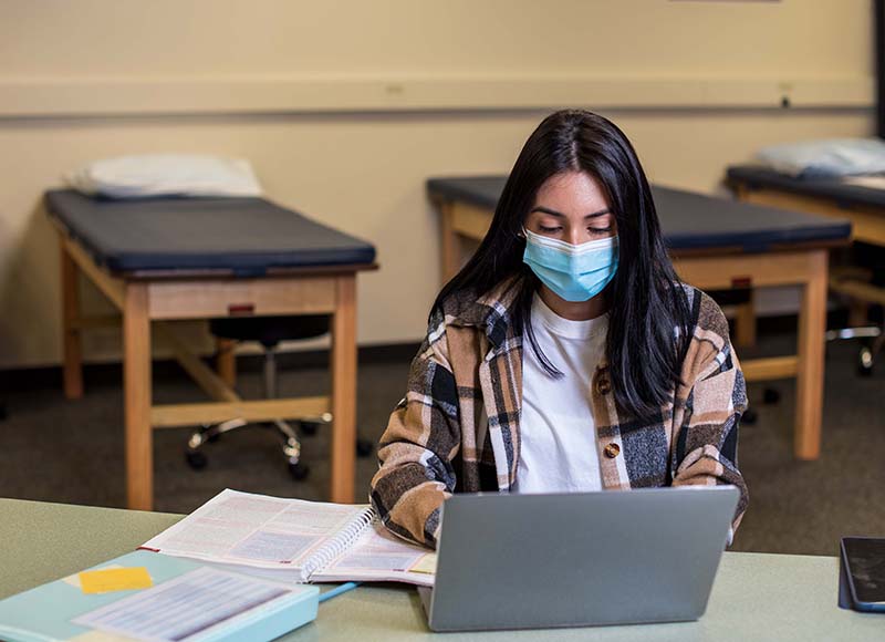 student typing on computer with mask